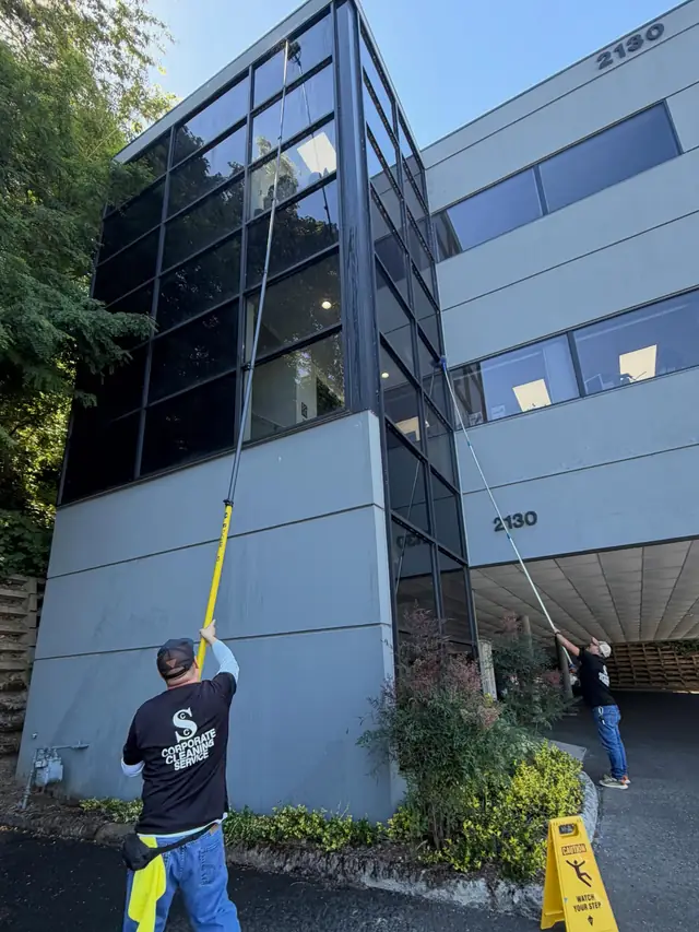 Two Corporate Cleaning Service crew members cleaning windows on a three storey office building